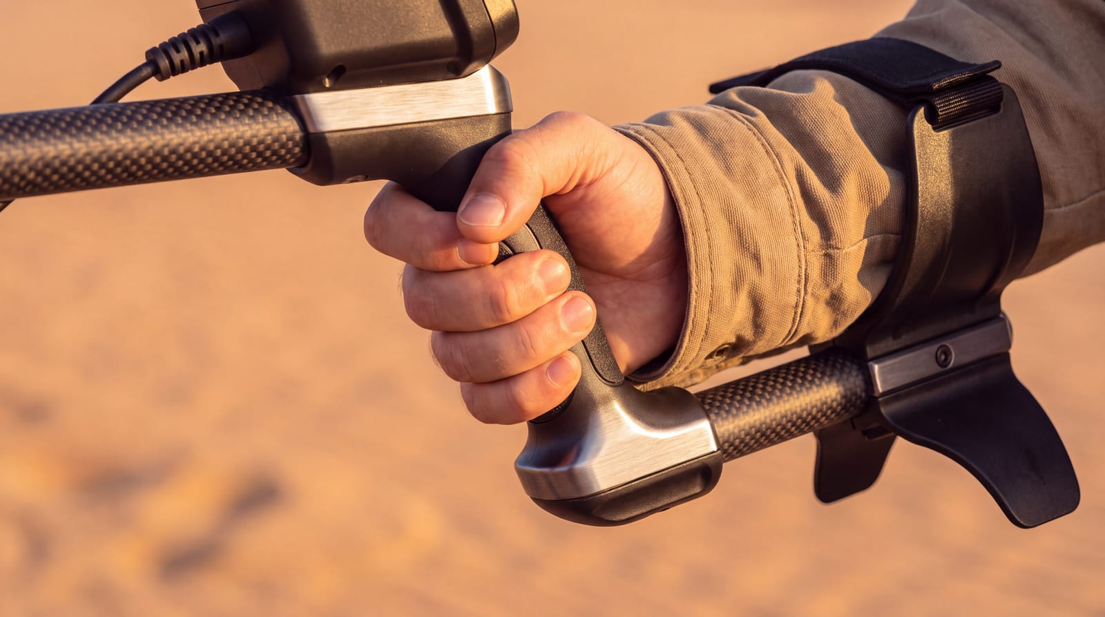 A detectorist's hand on the grip of a metal detector in the field.